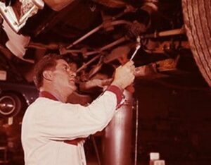 An elderly man inspecting or repairing the historic ceiling of a building, using a flashlight and tools, highlighting preservation efforts.