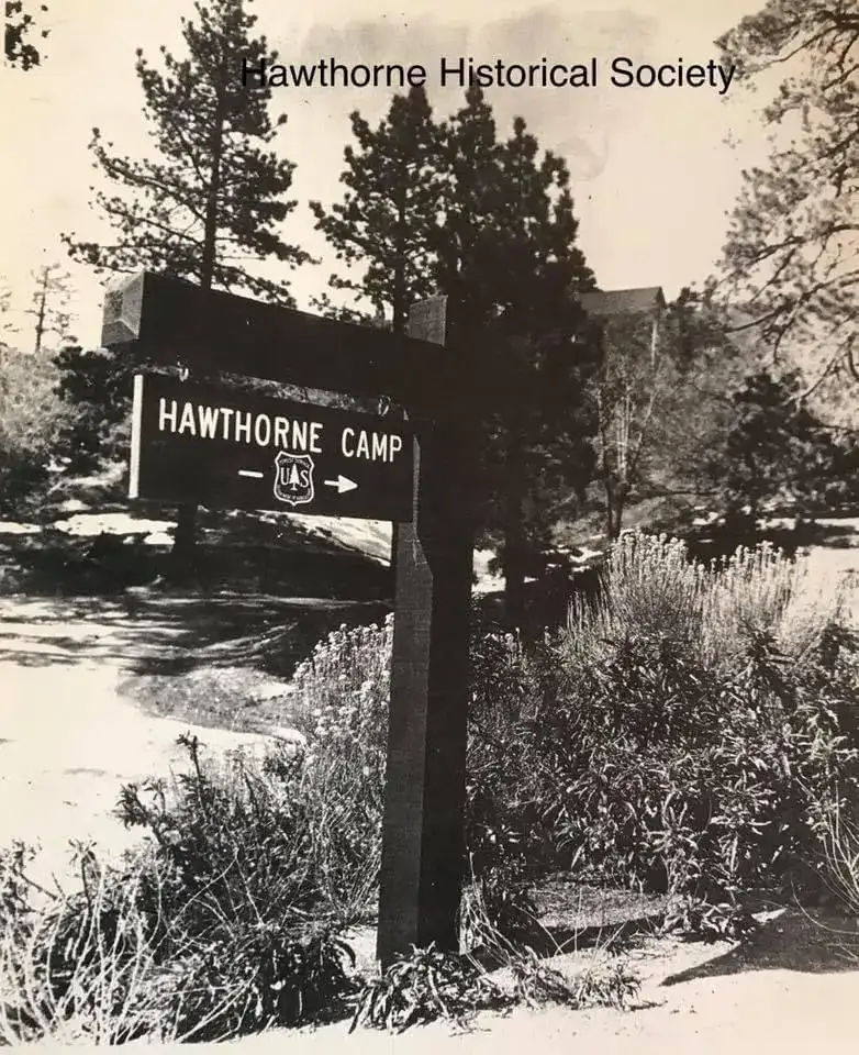 Vintage black and white photo of the Hawthorne Youth Camp sign surrounded by trees and nature, representing the connection to outdoor activities and community history.