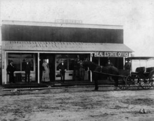 Historic black and white photo of Hawthorne Post Office and Real Estate Office with people and horse-drawn carriage, showcasing early 20th-century architecture.