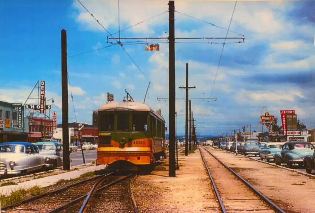 Vintage Hawthorne trolley car traveling along tracks in a busy mid-20th century street scene with cars and storefronts.