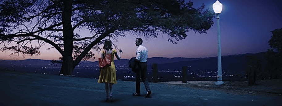 Two people talking at dusk with a scenic city view in the background.